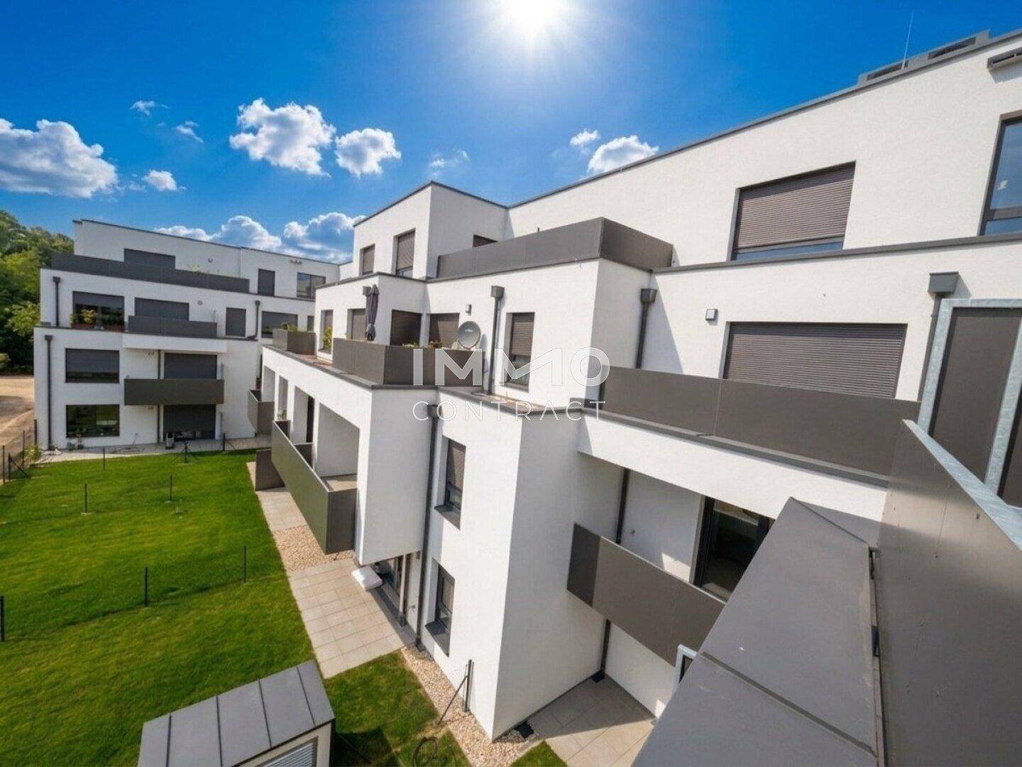 Architektonisch ansprechender Neubaukomplex mit Terrassen und Grünflächen unter blauem Himmel.