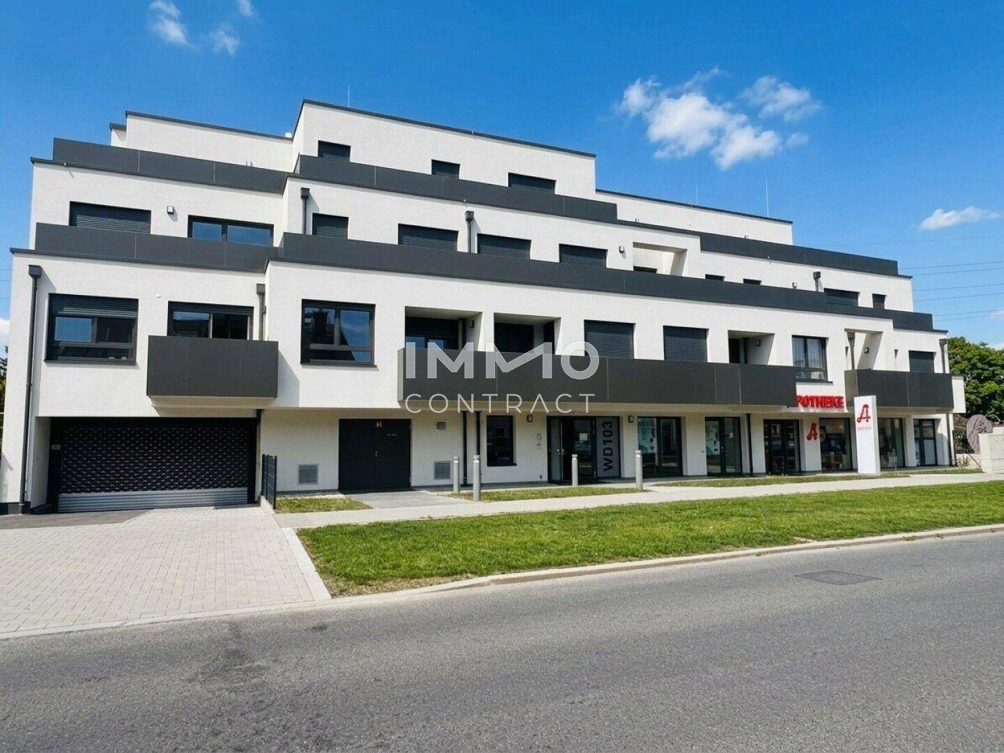 Moderne Wohnanlage mit Geschäften im Erdgeschoss und klaren architektonischen Linien unter blauem Himmel.