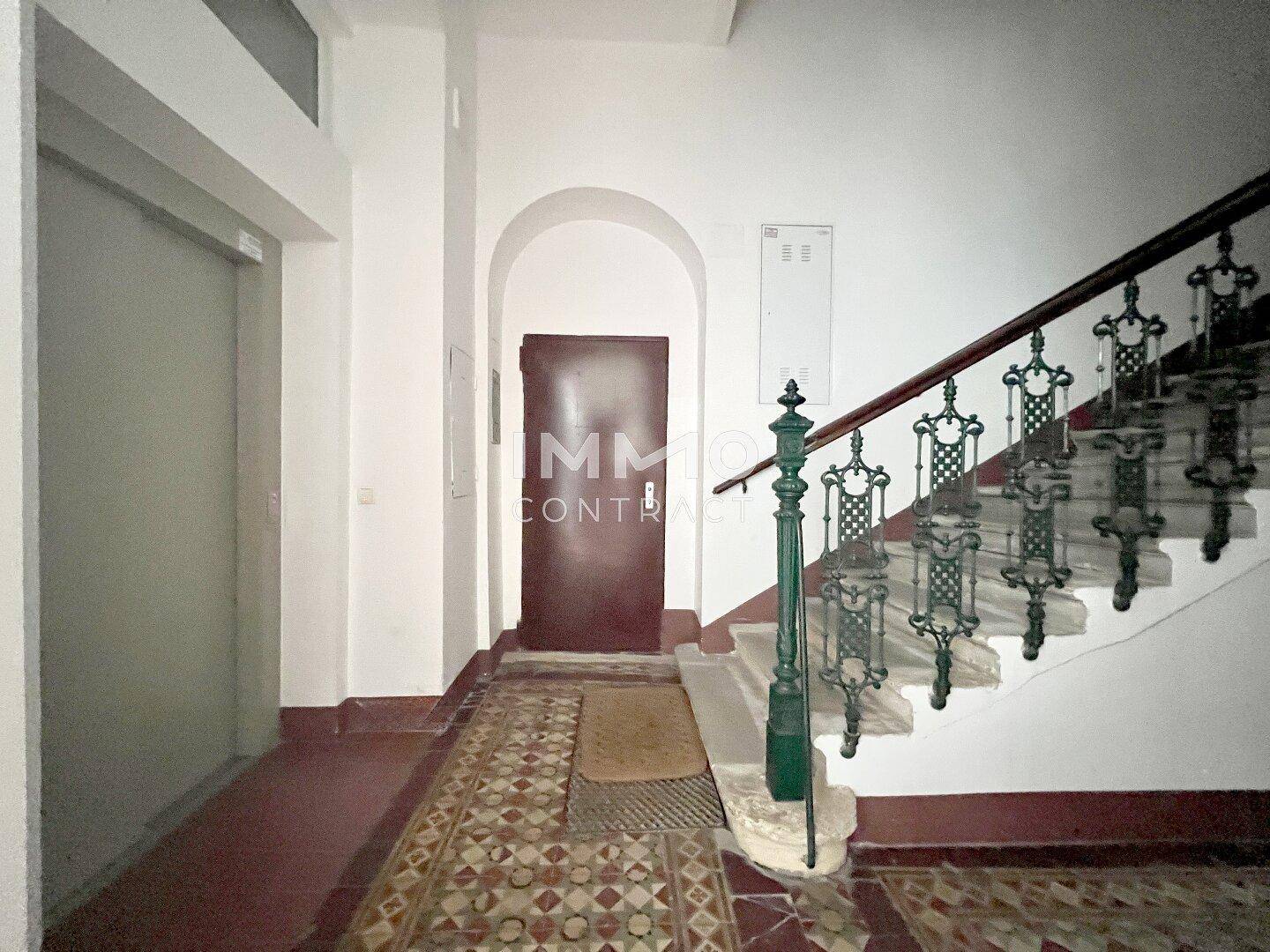 Historisches Treppenhaus mit kunstvollem Geländer und Aufzug in einem Altbau.