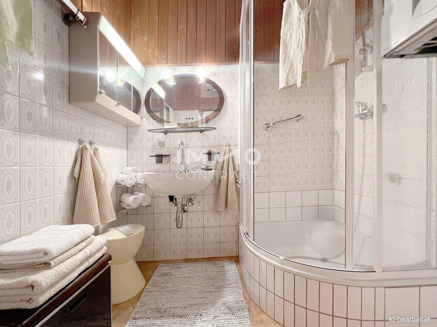 Badezimmer mit Duschkabine, WC, Waschbecken und gefliesten Wänden im 80er-Jahre-Stil.