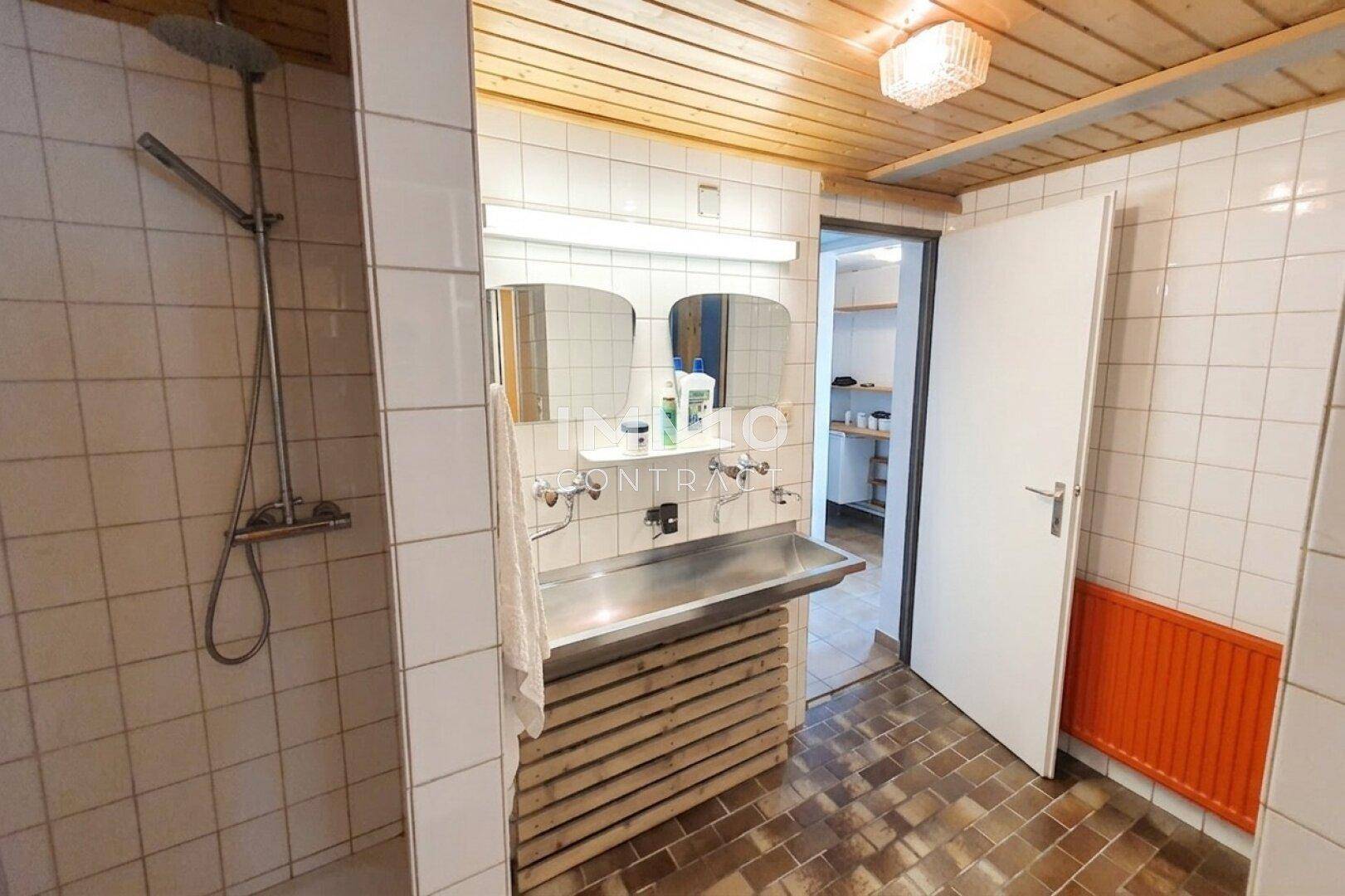 Einfaches Badezimmer mit Dusche, Doppelwaschbecken und Fliesenboden.