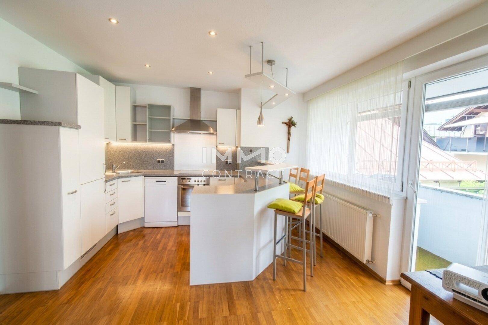 Moderne Einbauküche mit weißen Schränken, Frühstücksbar und Zugang zum Balkon.