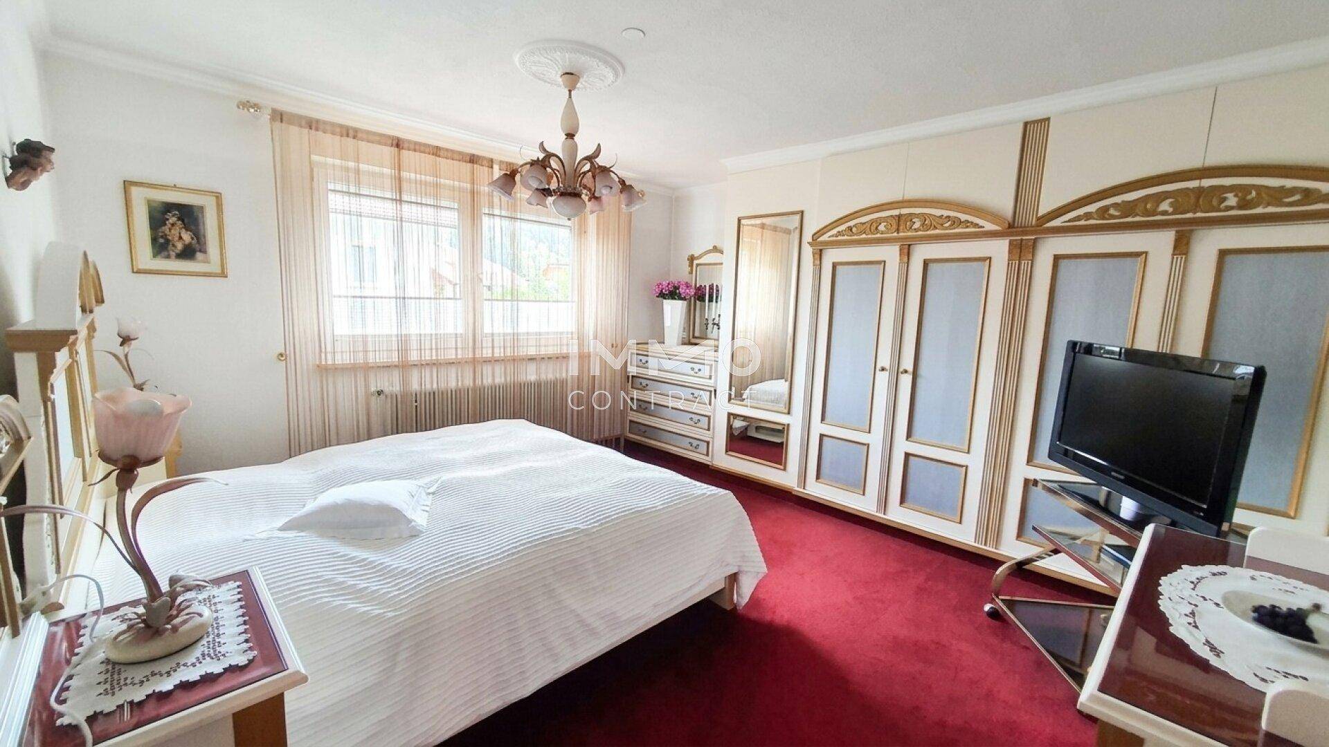 Geräumiges Schlafzimmer mit großem Bett, reich verzierten Schränken und Fenster.