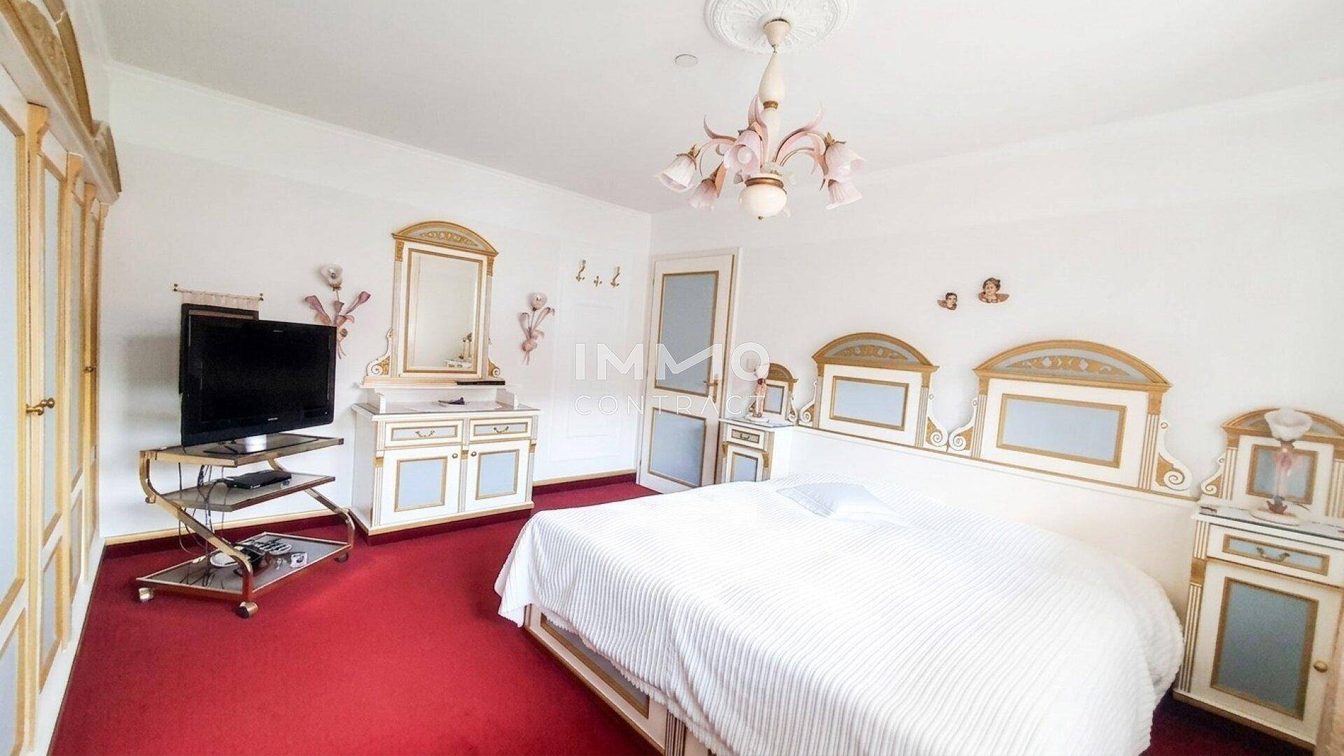 Elegantes Schlafzimmer mit rotem Teppich, opulenten Möbeln und Stuckdecke.