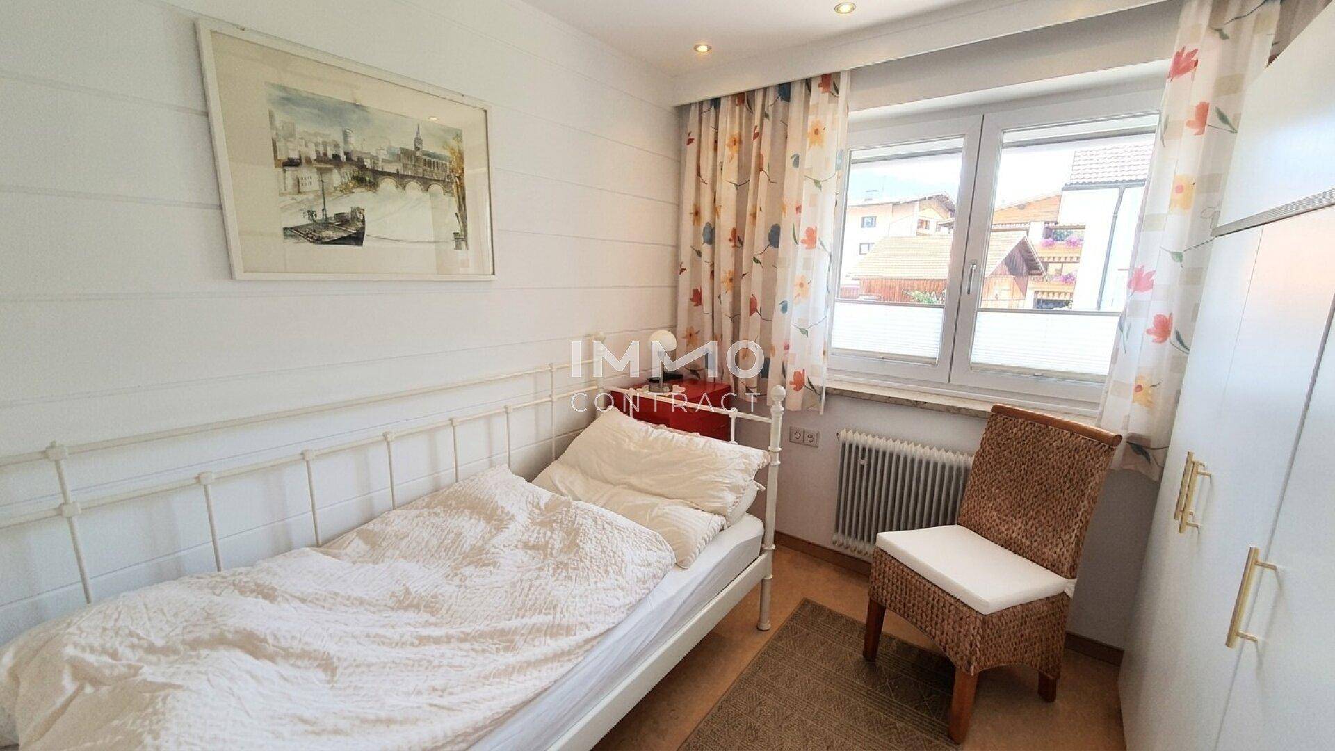 Gemütliches Einzelzimmer mit weißem Bett, Schrank und Fenster für natürliches Licht.