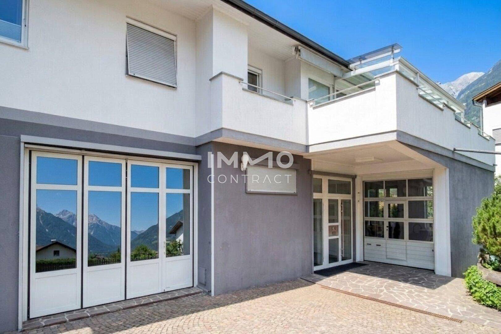Moderne Hausfassade mit Garageneinfahrt und großen Fenstern mit Bergblick.