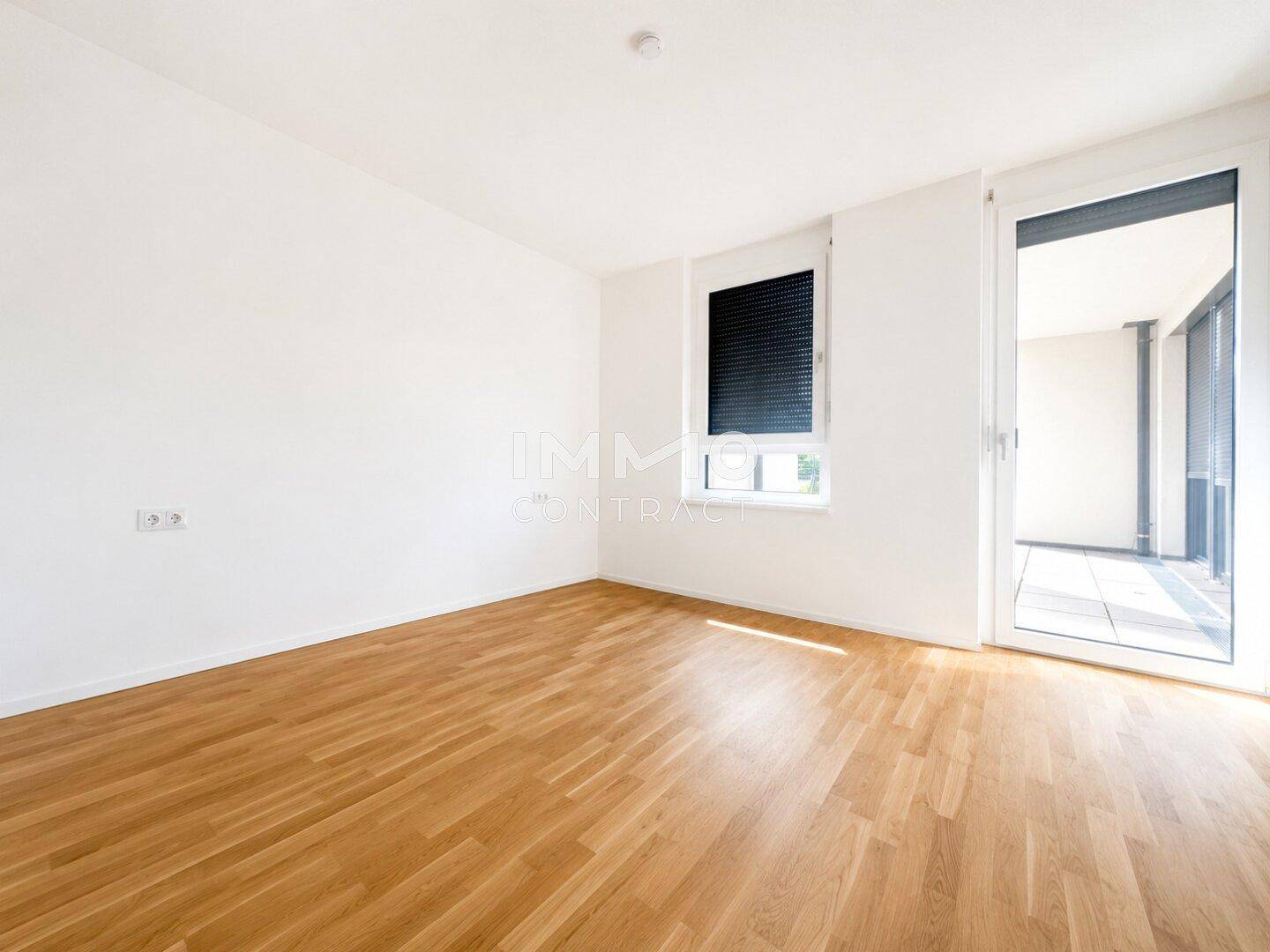 Helles Schlafzimmer mit Holzboden und Zugang zu einem Balkon, ausgestattet mit Rollläden für Privatsphäre.