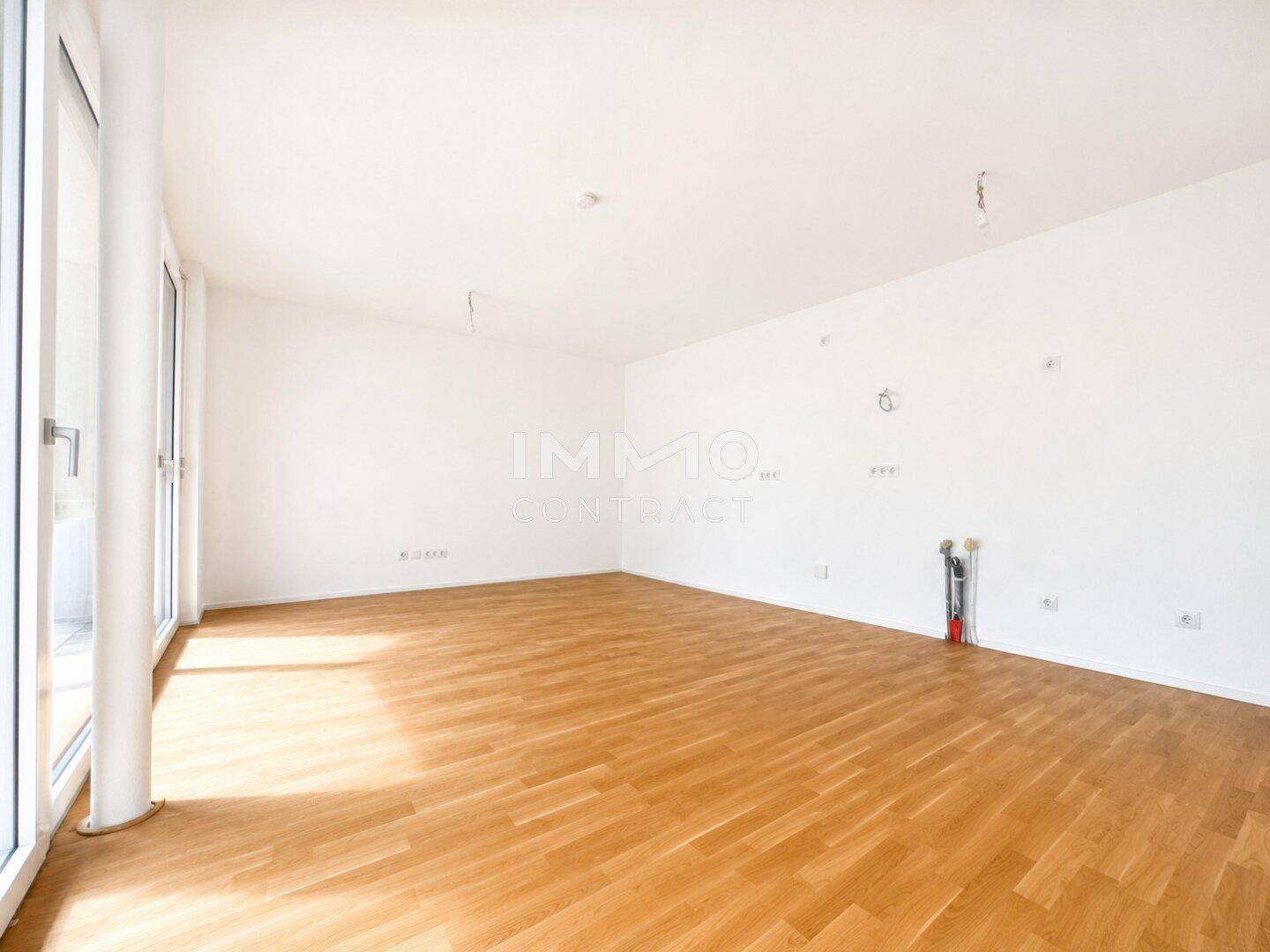 Heller, leerer Wohnraum mit großen Fenstern, Holzboden und viel Tageslicht, bereit zur individuellen Gestaltung.