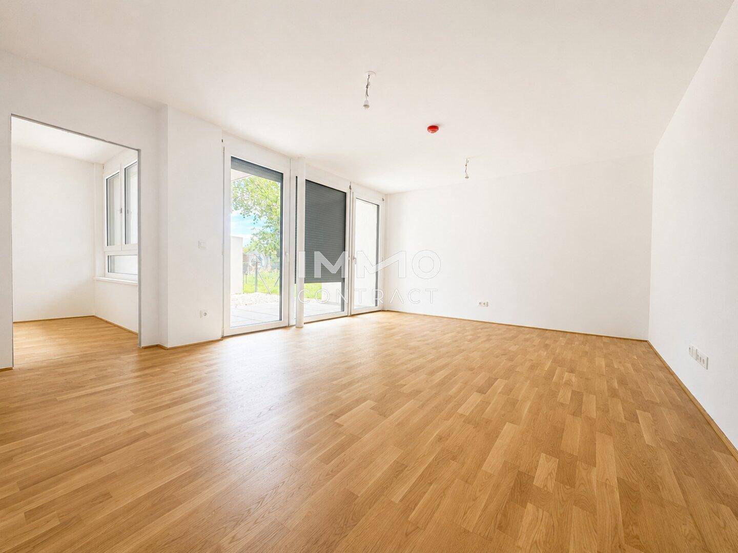 Helles, leeres Wohnzimmer mit Eichenparkettboden und großen Fenstern, die viel Tageslicht hereinlassen.