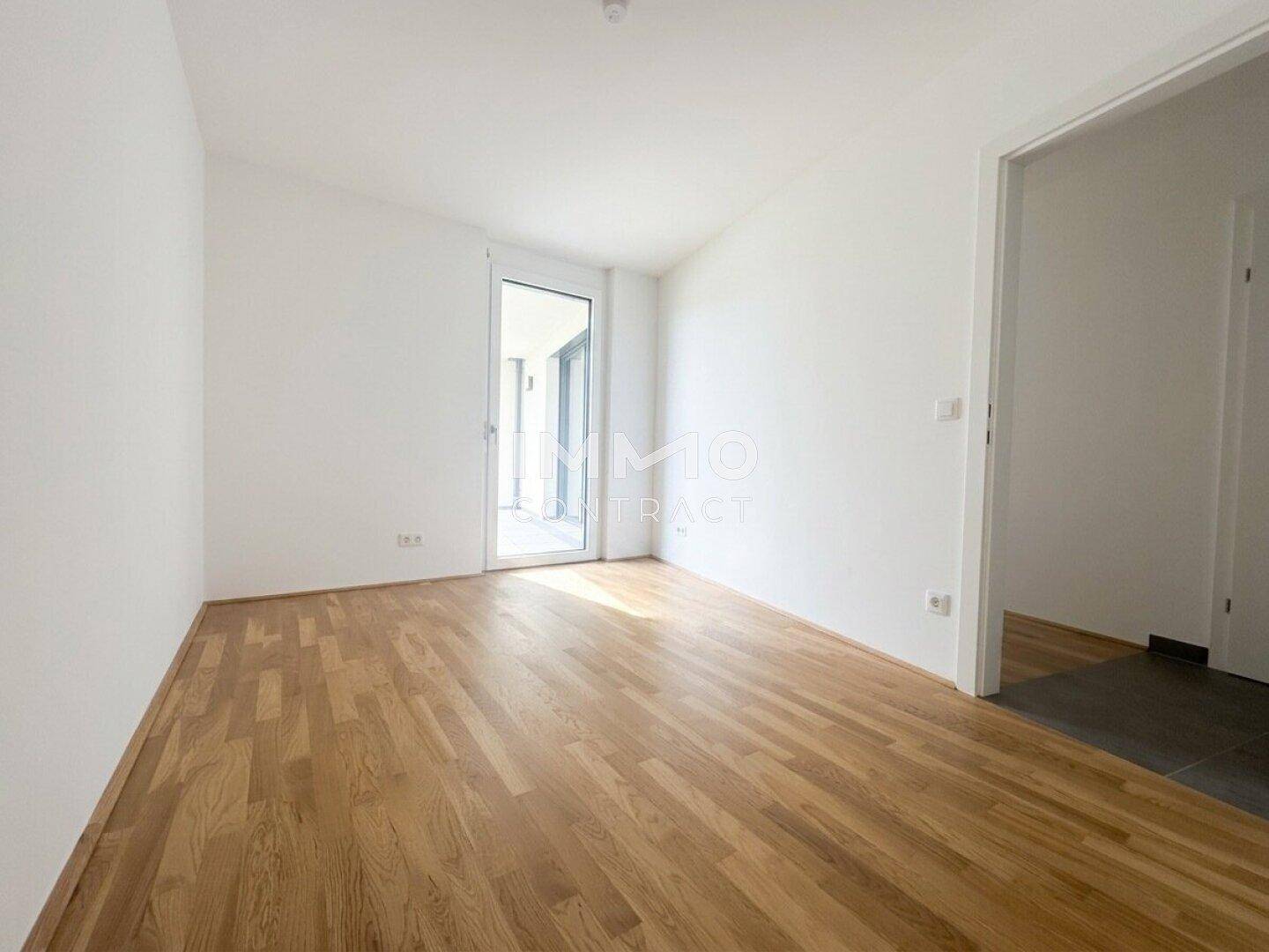Heller Wohnraum mit Parkettboden und Zugang zu einem Außenbereich durch eine Glastür.