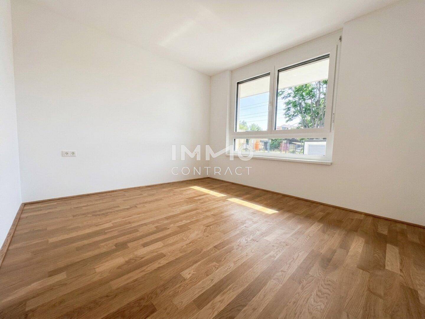 Schlafzimmer mit hellem Parkettboden und großem Fenster, das viel Tageslicht hereinlässt.