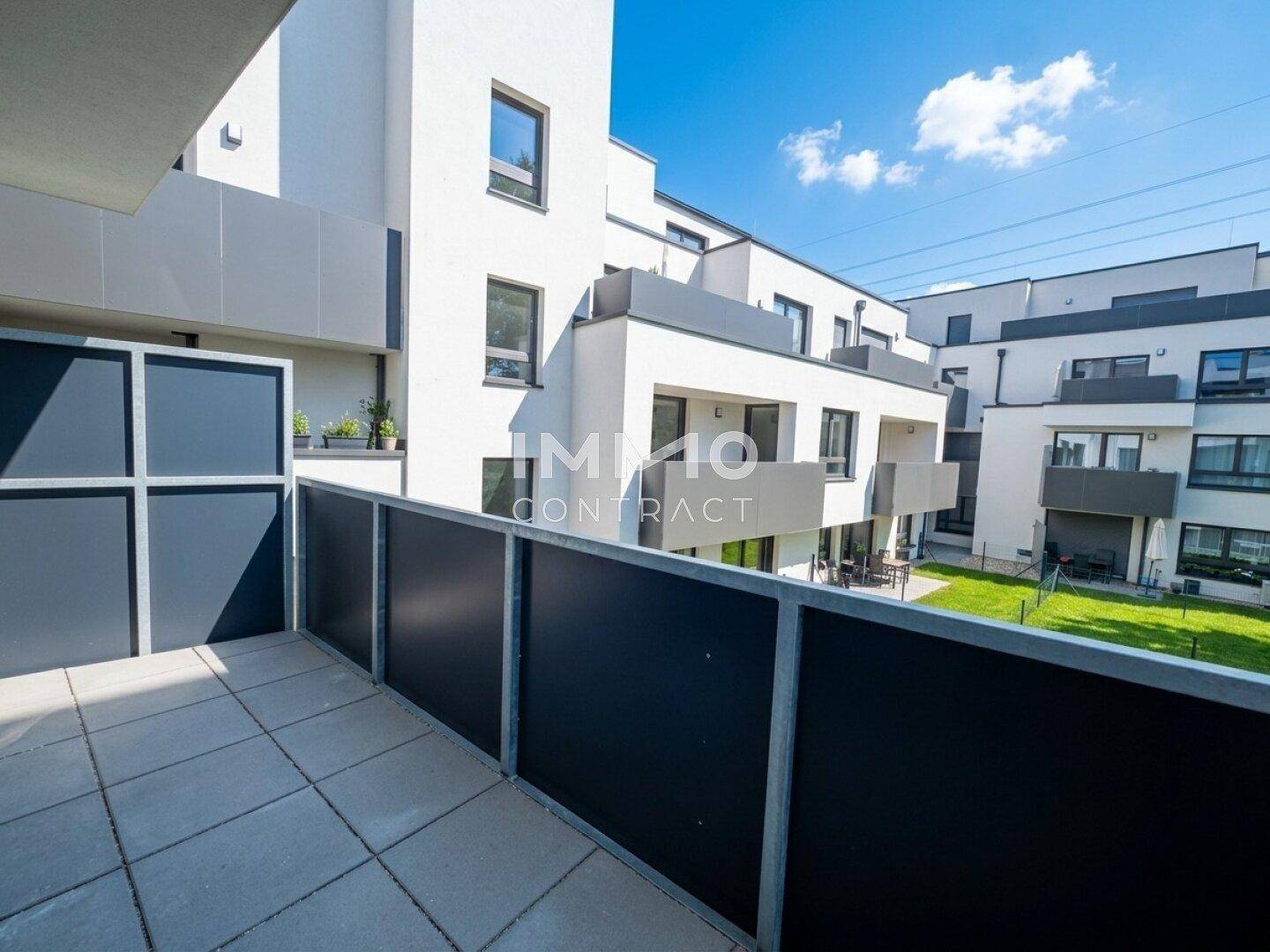 Balkon mit Fliesenboden und Ausblick auf die moderne Wohnanlage und den Gartenbereich.