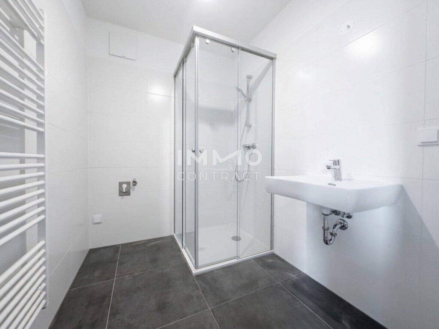 Modernes Badezimmer mit Duschkabine, weiß gefliesten Wänden und dunklem Fliesenboden.