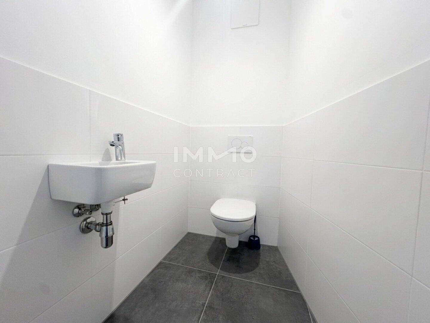 Gäste-WC mit wandhängender Toilette, modernem Waschbecken und dunklem Fliesenboden.
