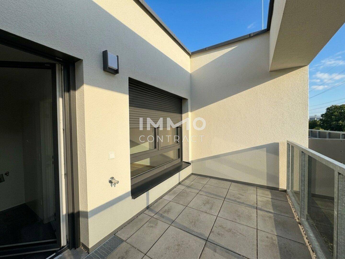 Heller Balkon mit Fliesenboden, Glasgeländer und Blick auf die Umgebung.
