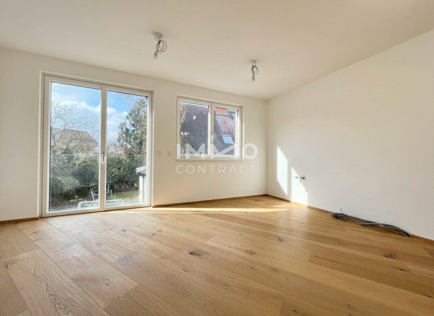 Lichtdurchfluteter Raum mit Holzparkettboden und großzügigem Zugang zu einem Garten oder einer Terrasse.