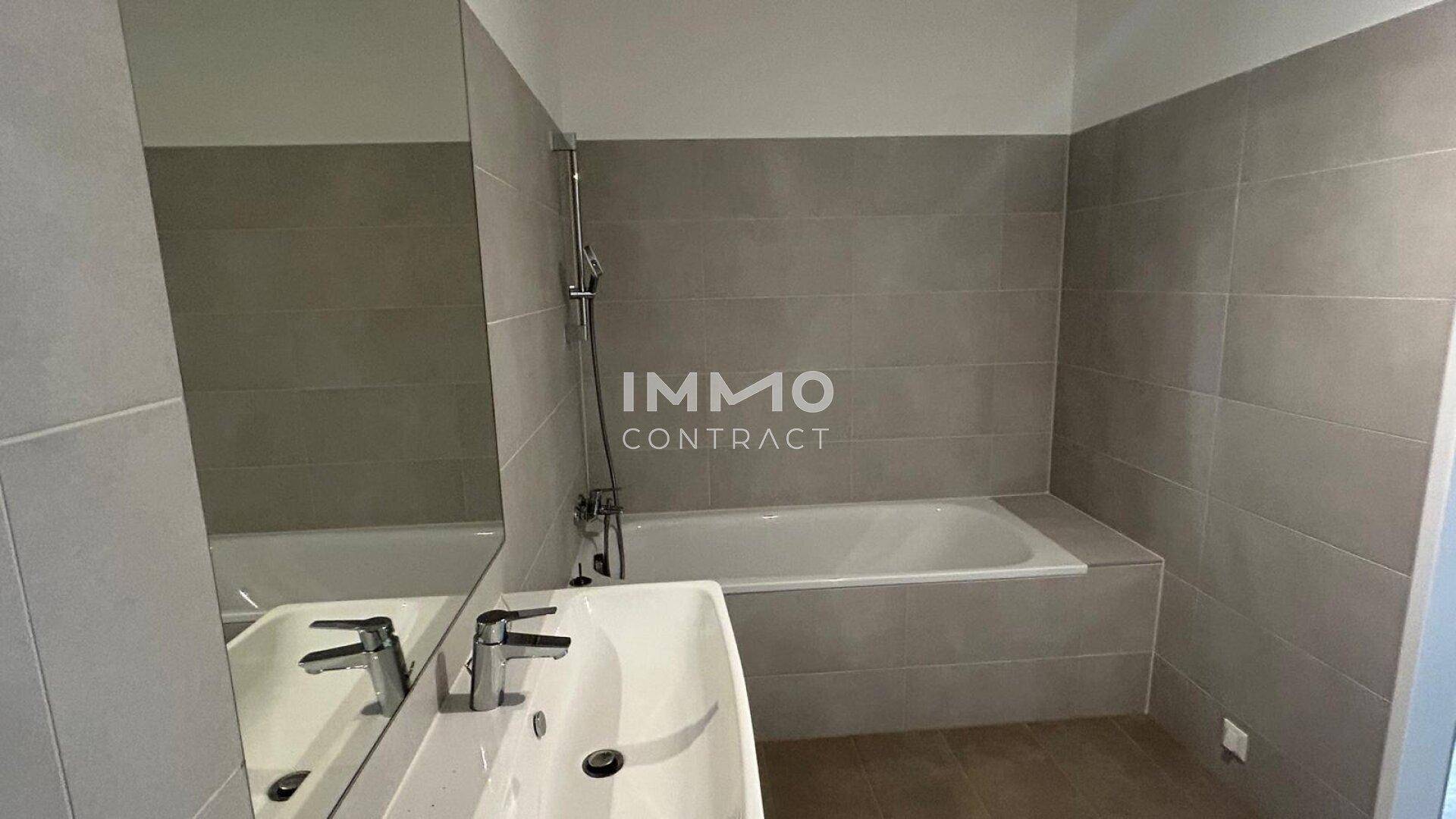 Badezimmer mit Badewanne, Waschbecken und großem Spiegel, in hellen Grautönen gehalten.