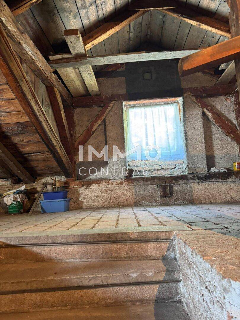 Unausgebauter Dachboden mit sichtbaren Holzbalken und einem kleinen Fenster, bietet Ausbaupotenzial.