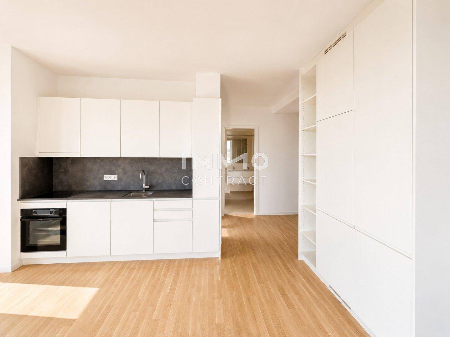 Moderne Küchenzeile mit weißen Schränken, dunkler Arbeitsplatte und integriertem Backofen.