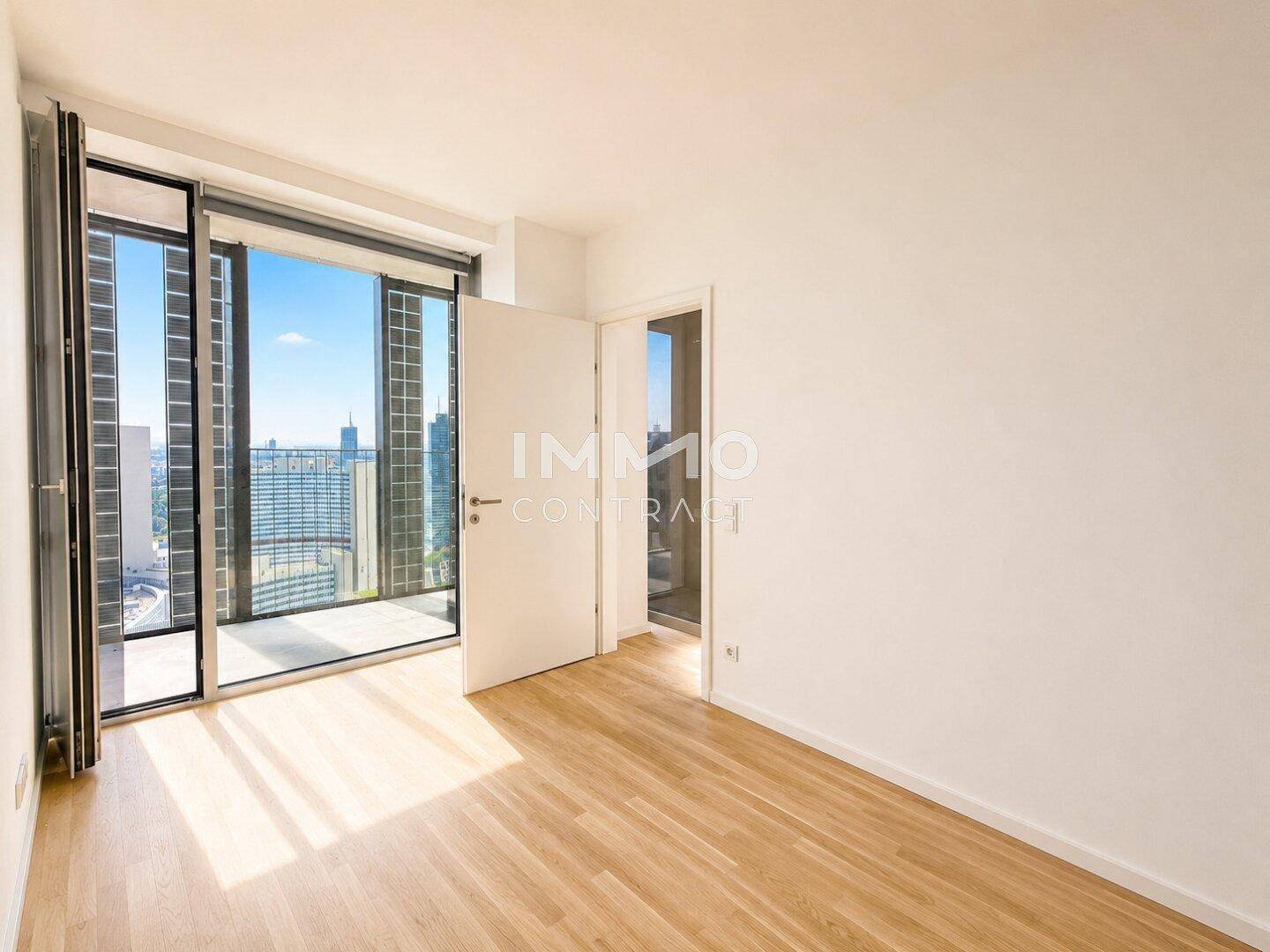 Heller Raum mit Parkettboden, Zugang zum Balkon und Panoramablick über die Stadt.