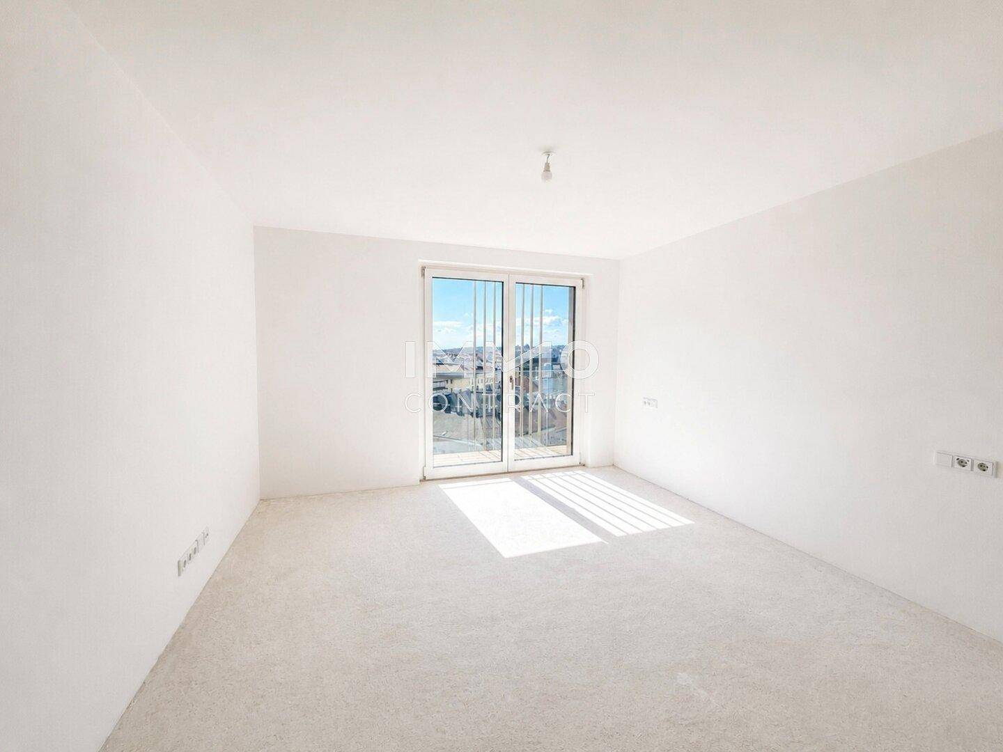 Helles, leeres Zimmer mit großem Fenster und Blick auf die Umgebung.