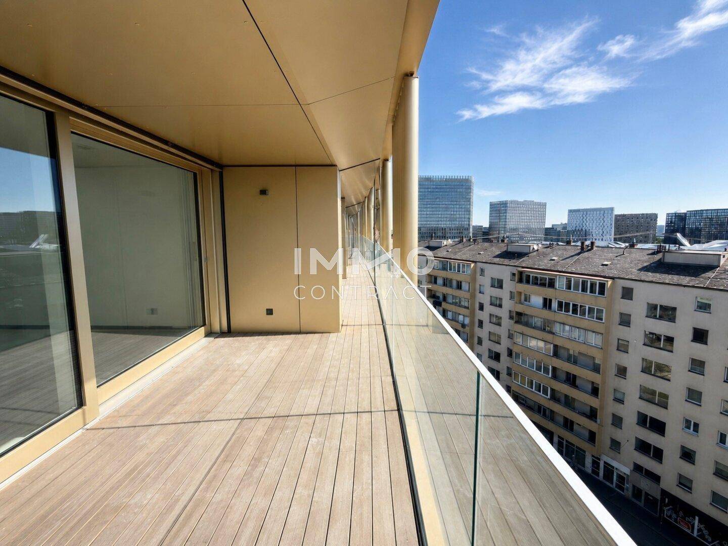 Geräumiger Balkon mit Holzdeck und Glasgeländer, bietet einen weiten Blick über die Stadt.