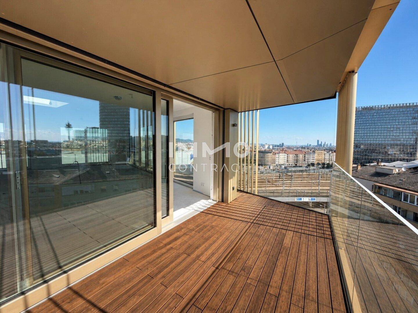 Geräumiger Balkon mit Holzboden und Glasbrüstung, bietet einen weiten Stadtblick.