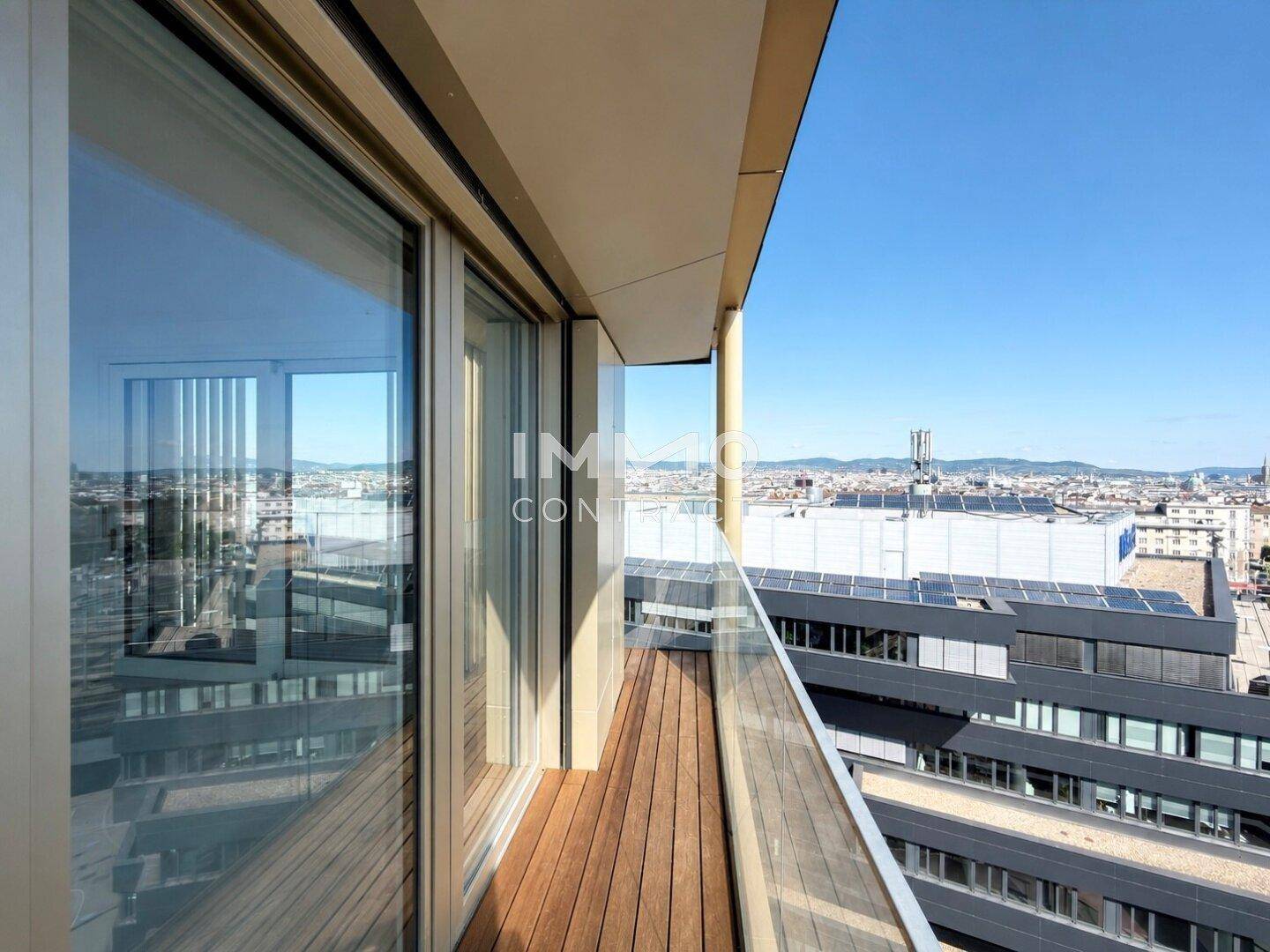 Moderner Balkon mit Holzfußboden, Glasgeländer und Panoramablick über die Stadt.