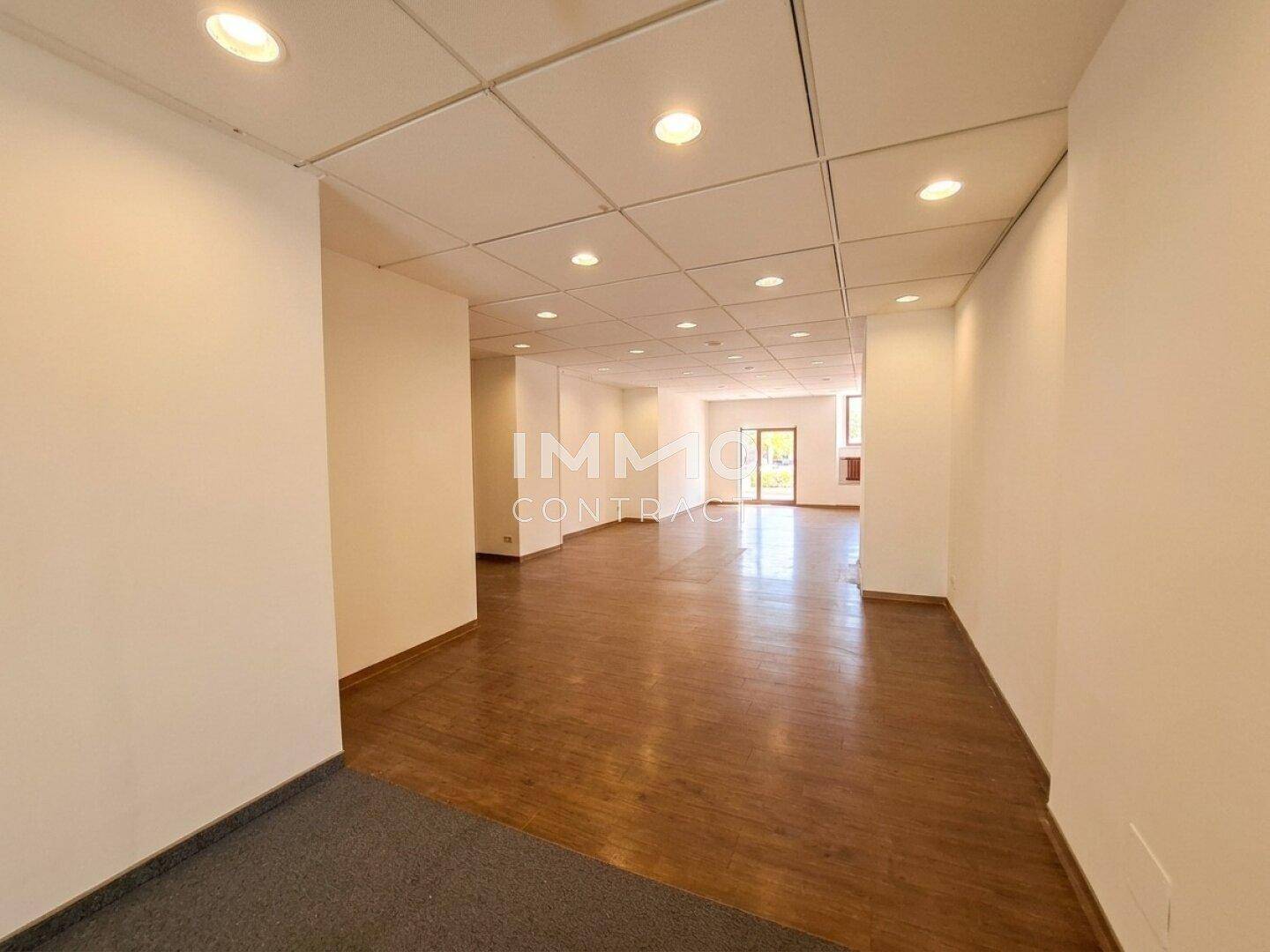 Großer, leerer Gewerberaum mit Holzfußboden und Rasterdecke mit integrierter Beleuchtung.