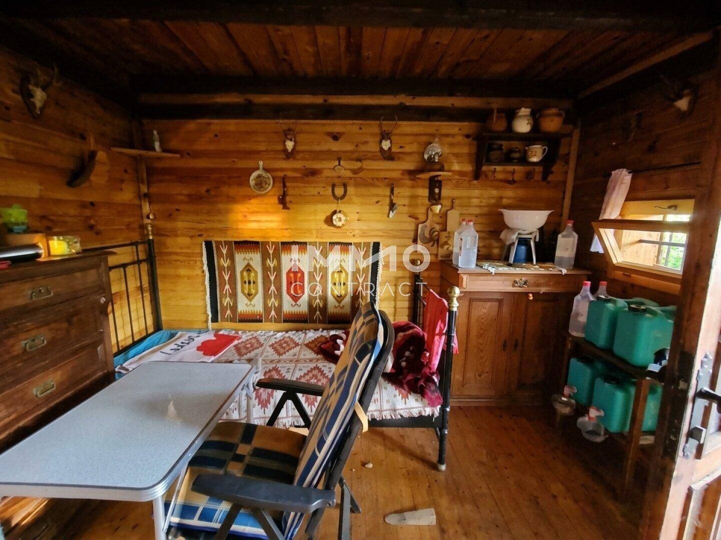 Rustikaler Wohn-Schlafbereich mit Holzwänden, einfachen Möbeln und Hirschgeweihen.