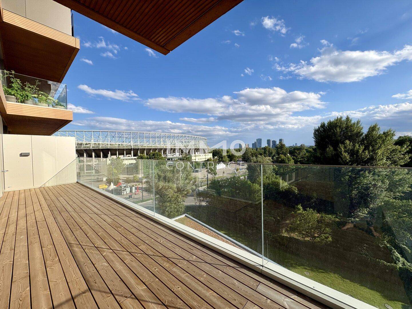 Moderne Holzterrasse mit Glasgeländer und Blick auf das Stadion und die Stadt.