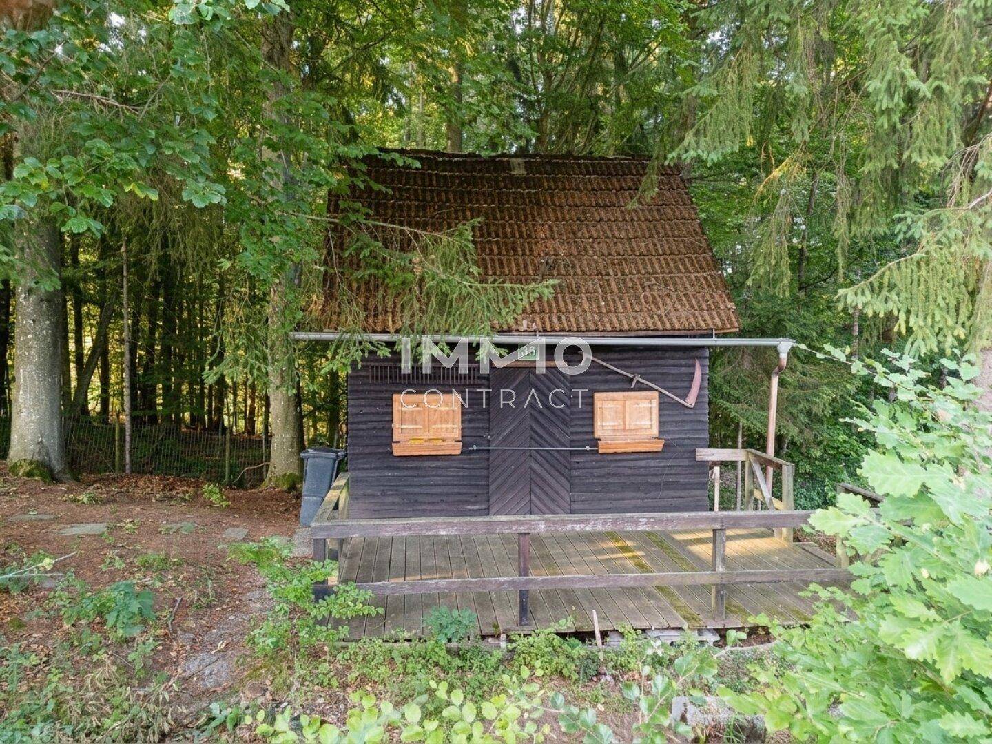 Einfache Holzhütte mit braunem Ziegeldach und kleiner Holzveranda im Grünen.