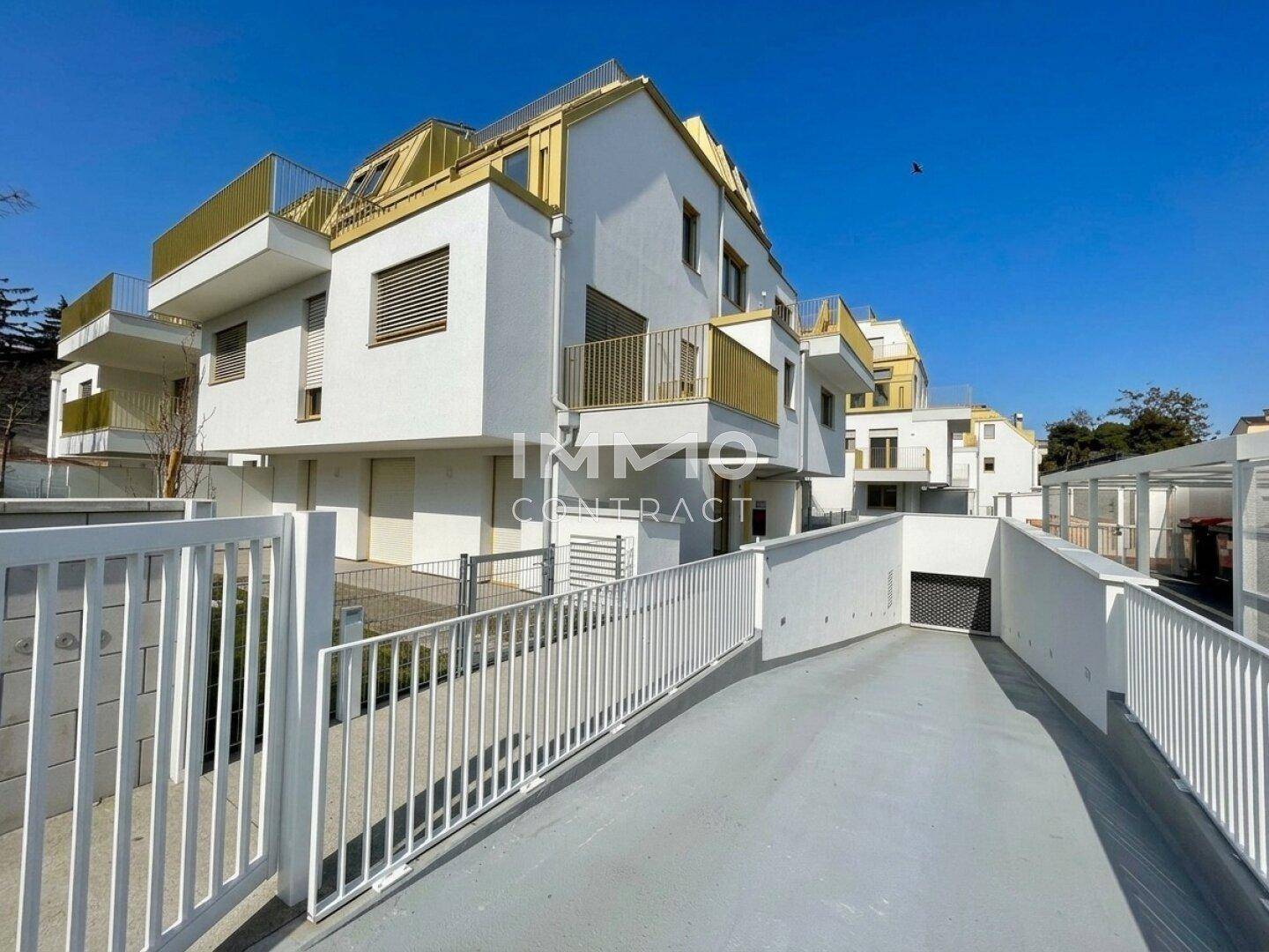 Moderne Wohnanlage mit weißer Fassade, goldenen Akzenten und Zufahrt zur Tiefgarage.