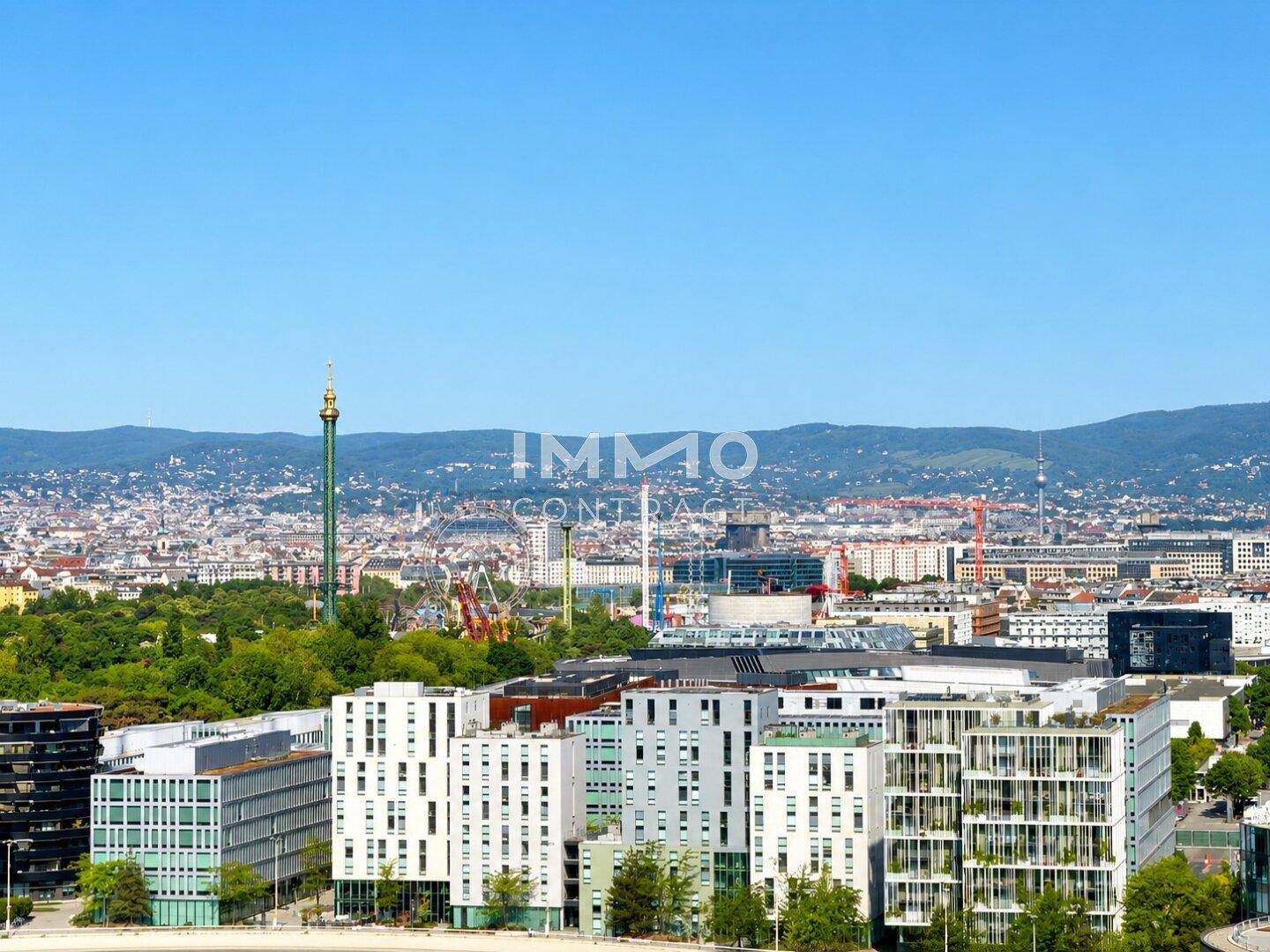 Weitläufiger Stadtblick mit markanten Gebäuden und dem Prater, umgeben von Hügeln am Horizont.
