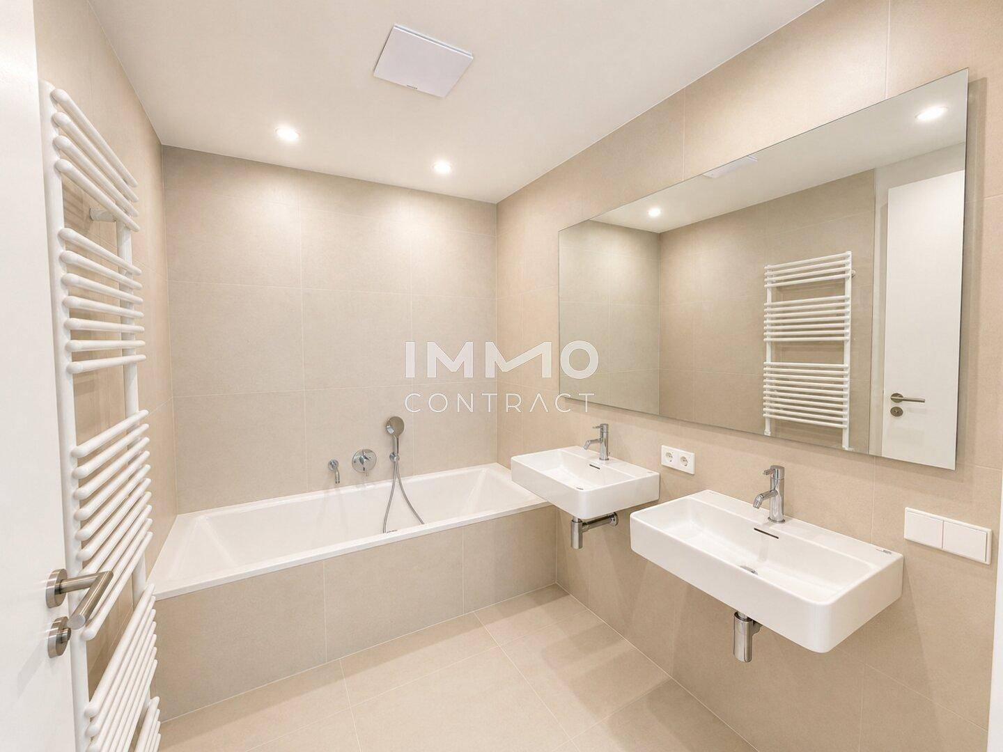 Modernes Badezimmer mit Badewanne, Doppelwaschbecken und beheiztem Handtuchhalter, in hellen Fliesen gehalten.