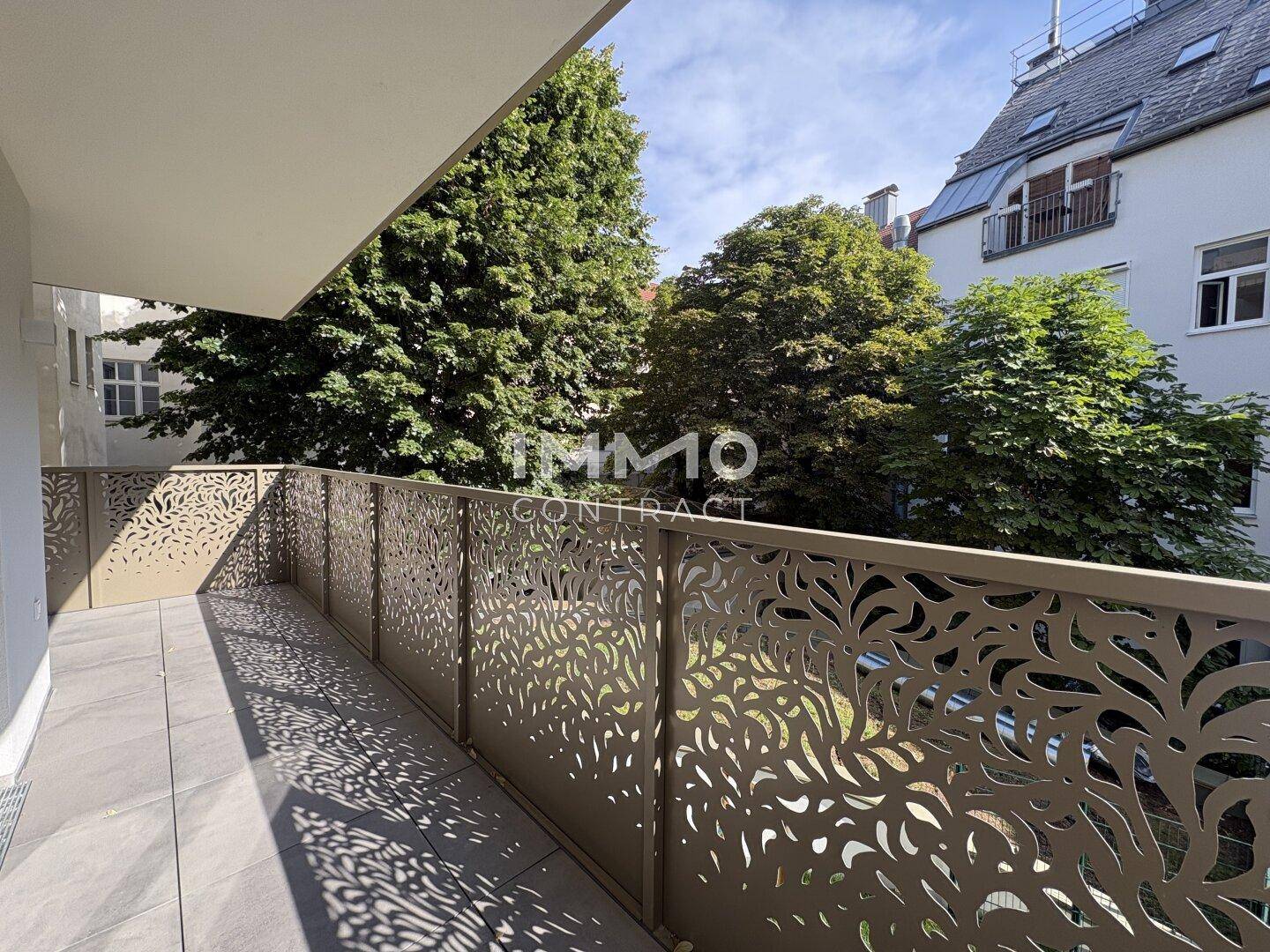 Geräumiger Balkon mit modernem Geländer und Fliesenboden, umgeben von grünen Bäumen und Gebäuden.