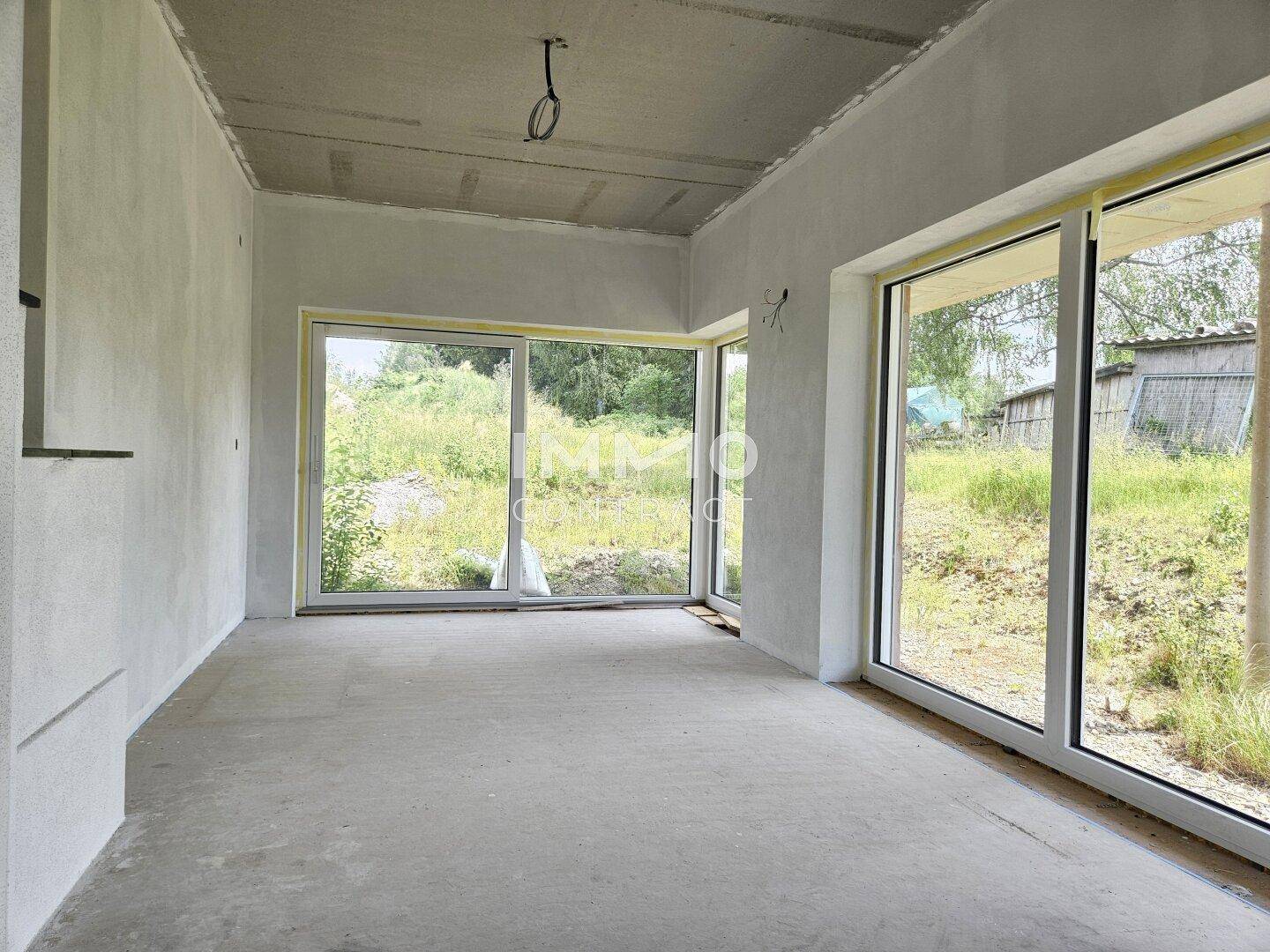 Heller Rohbau eines Raumes mit großen Schiebefenstern und Blick ins Grüne.