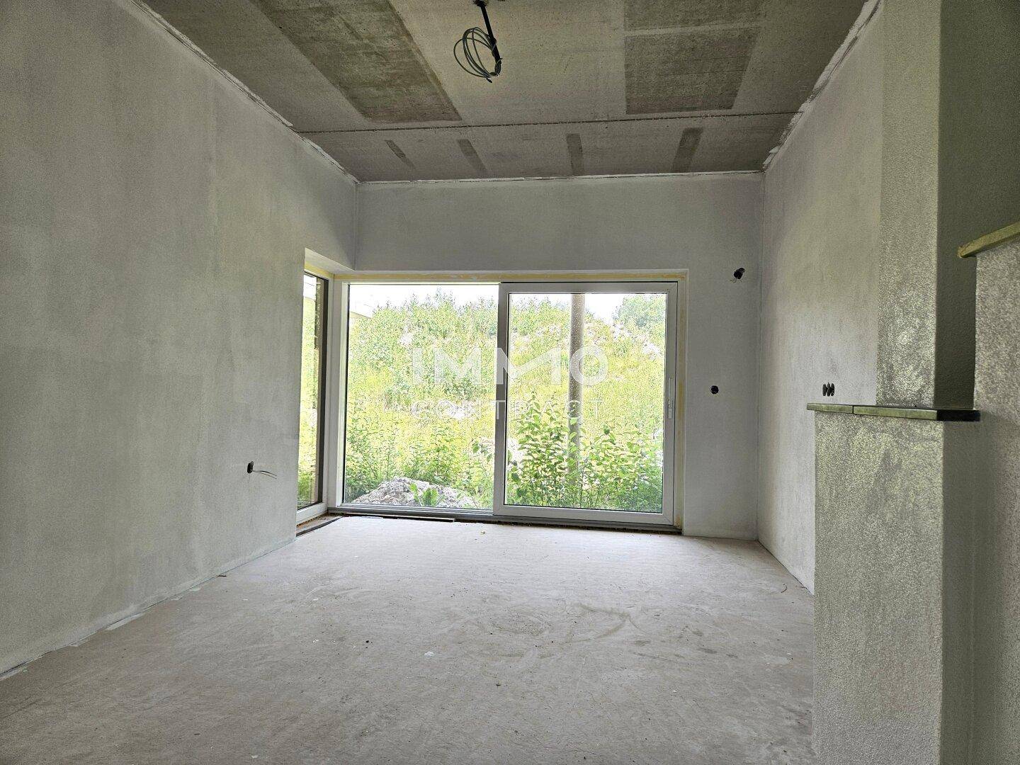 Heller Rohbau eines Zimmers mit großer Fensterfront und Blick auf die Natur.