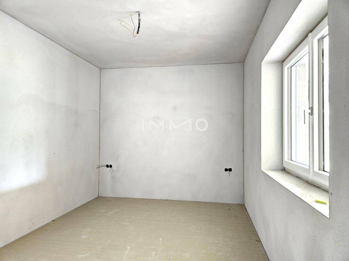 Unfertiges Schlafzimmer im Rohbau mit einem Fenster und vorbereiteten Steckdosen.