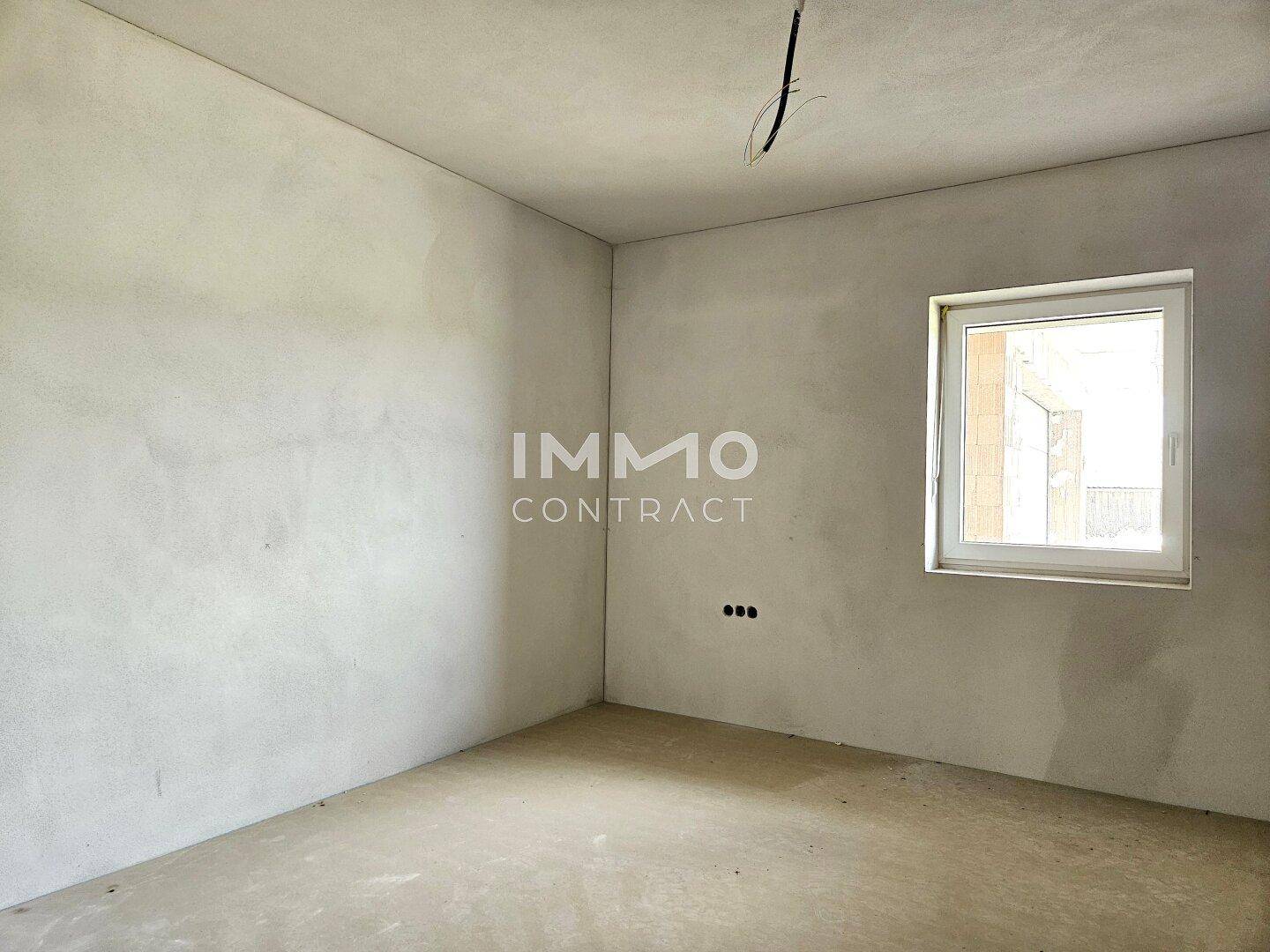 Rohbau eines Zimmers mit Fenster und glatt verputzten Wänden, bereit für den Ausbau.
