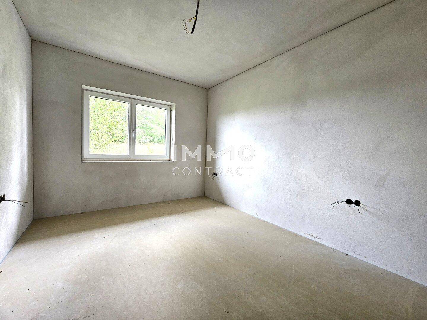 Helles Schlafzimmer im Rohbau mit Fenster und Blick ins Grüne.