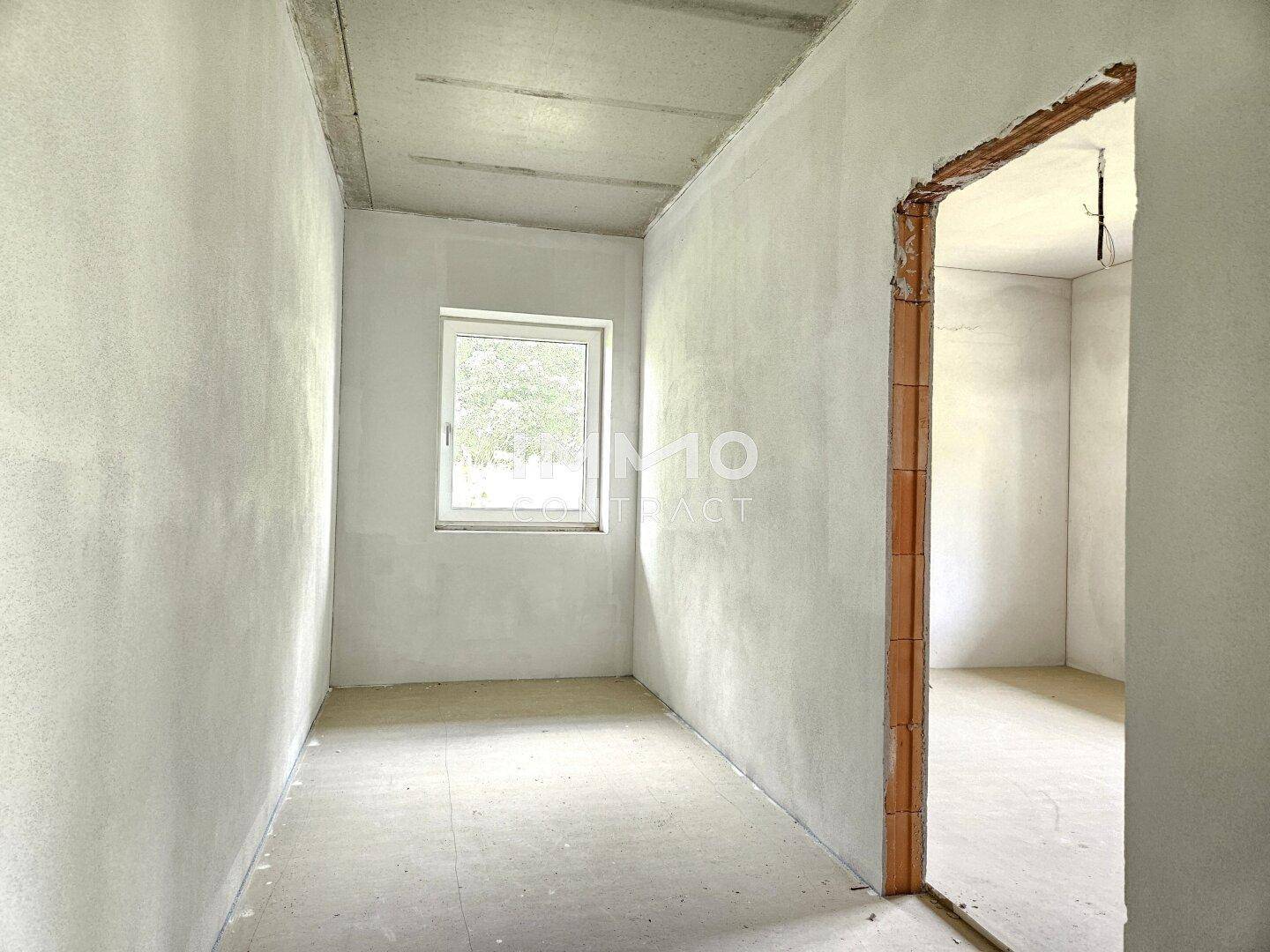 Unfertiger Flur im Rohbau mit Fenster und Zugang zu weiteren Räumen.