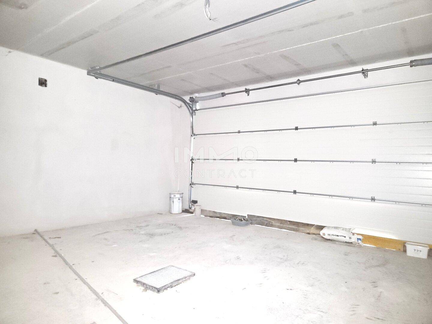 Unfertige Garage mit Sektionaltor und Betonboden, bereit für den Ausbau des Hauses.