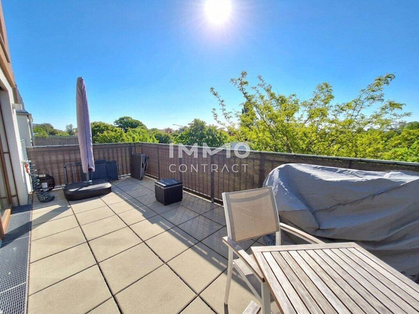 Geräumige Terrasse mit Sitzgelegenheiten und Sonnenschirm, umgeben von Bäumen.