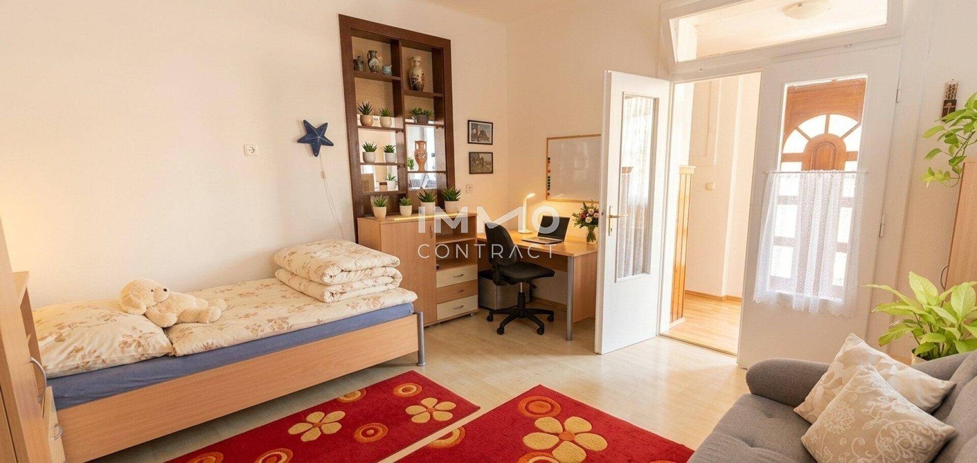 Helles Schlafzimmer mit Einzelbett, Schreibtisch und Zugang zu einem weiteren Raum.