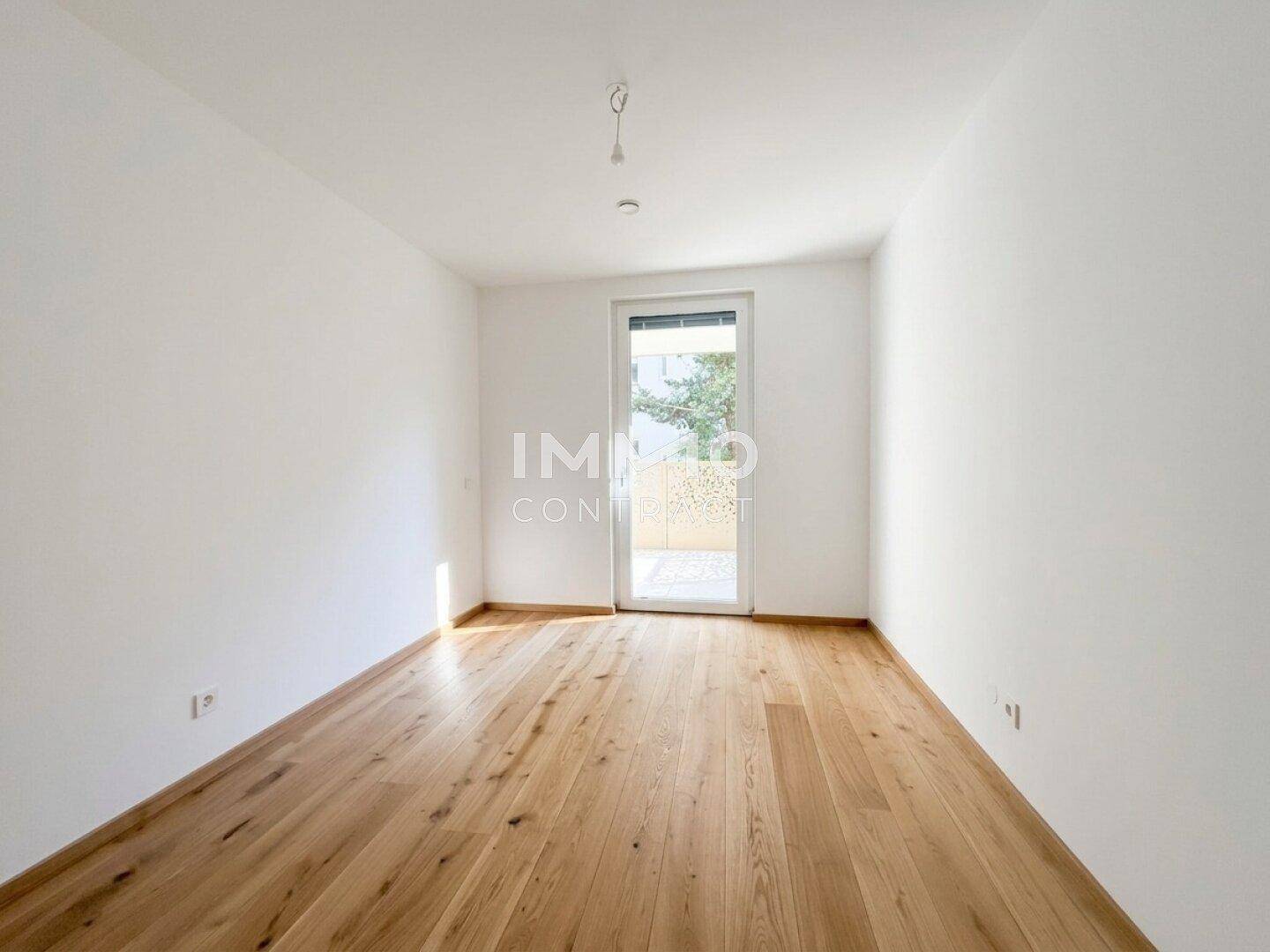 Heller, leerer Raum mit Holzboden und Zugang zu einem Außenbereich.