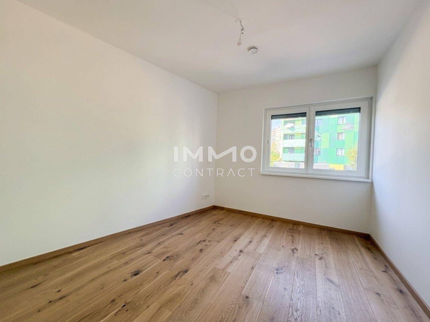 Heller, leerer Raum mit Holzboden und Fenster mit Blick auf die Umgebung.