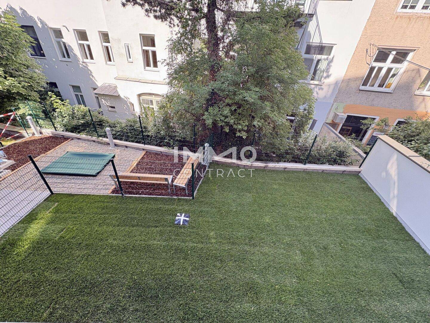 Kleiner Gartenbereich mit Kunstrasen, umzäunt und mit einfacher Bepflanzung.