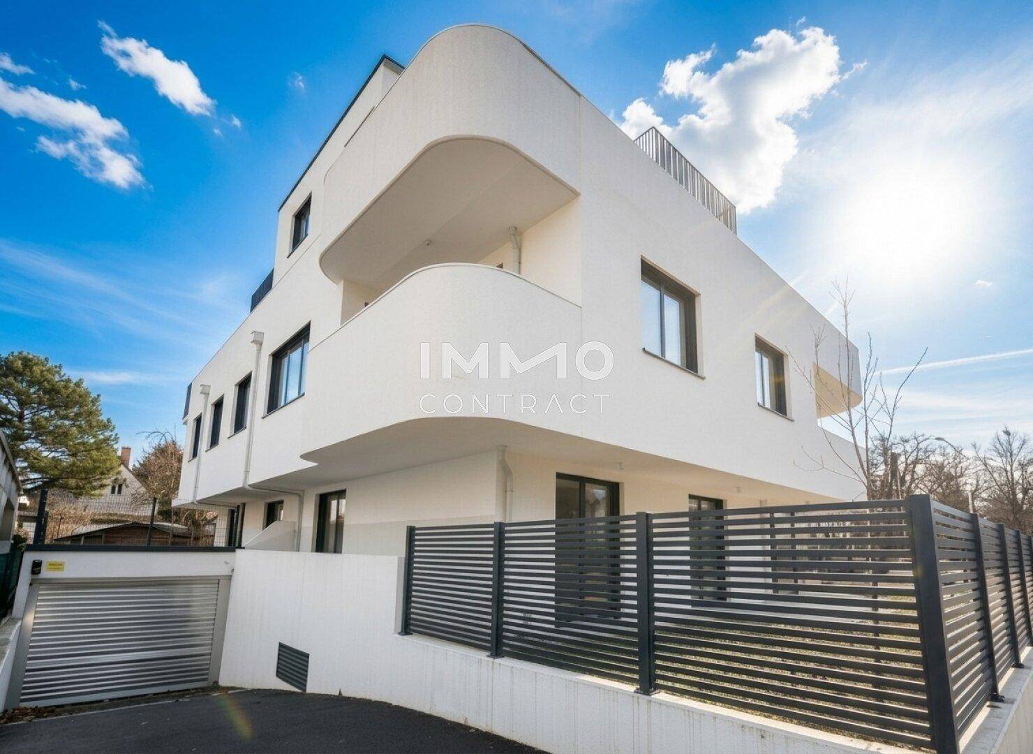 Moderne weiße Wohnanlage mit geschwungenen Balkonen und großen Fenstern.
