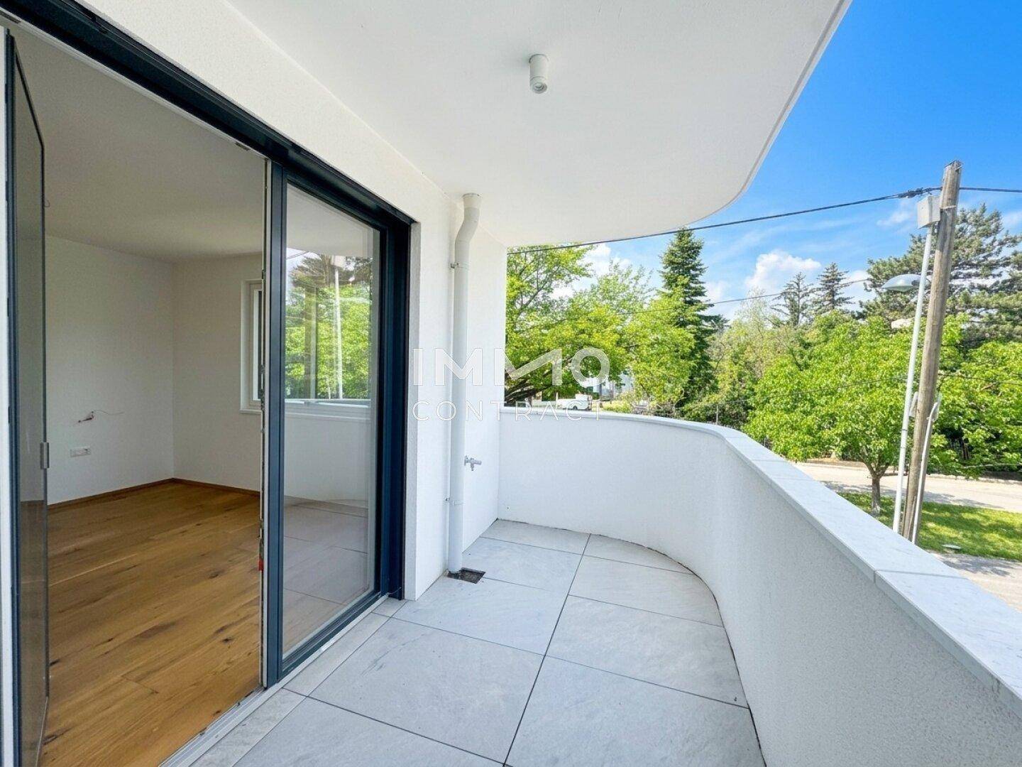 Geräumiger Balkon mit Fliesenboden und Zugang zu einem leeren Zimmer mit Holzparkett.
